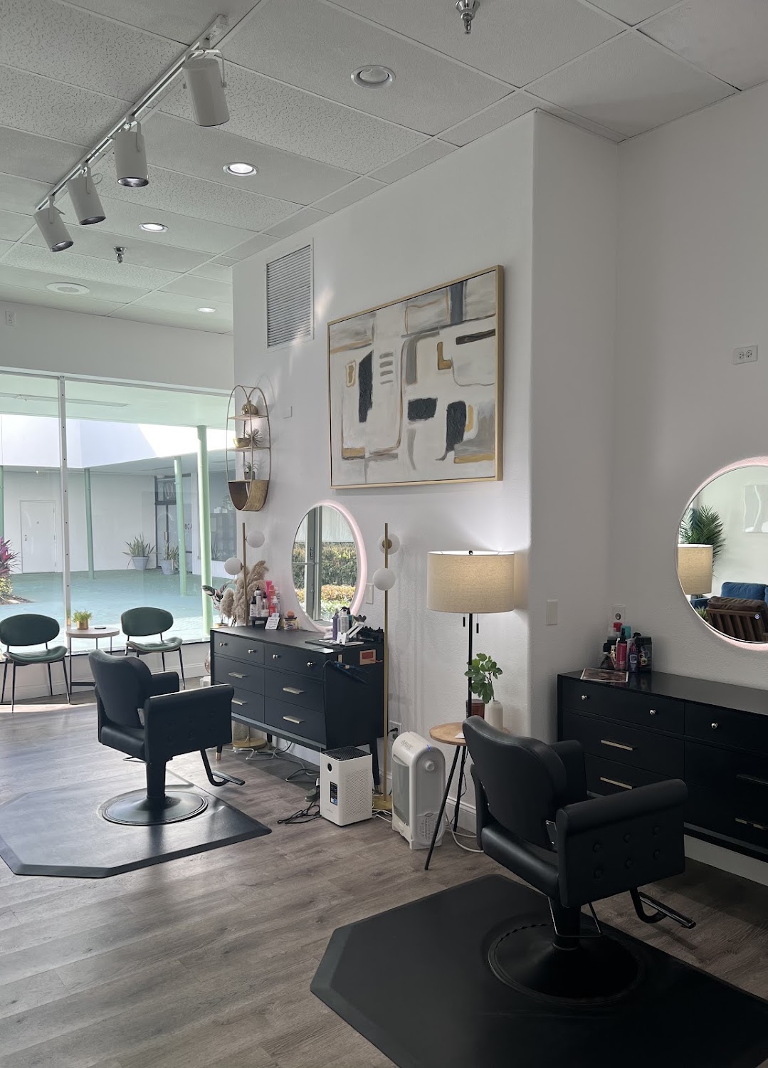 Interior of The Strand Salon: bright styling stations with round backlit mirrors, black chairs and floor-to-ceiling windows onto a courtyard.